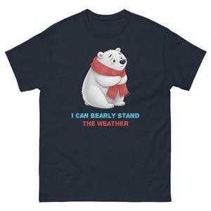 May include: Navy blue t-shirt featuring a cartoon polar bear wearing a red scarf, with the text "I CAN BEARLY STAND THE WEATHER" in blue and red. The bear has a sad expression, and the shirt is a classic crew neck style.