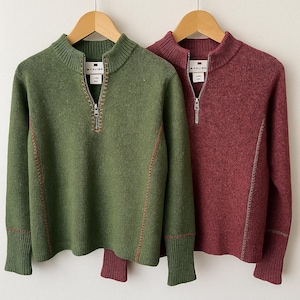 May include: Two sweaters hanging on wooden hangers. One is olive green, the other is burgundy. Both have a half-zip closure, ribbed cuffs, and the brand name "MODLISO" on a tag. The sweaters have a high collar and are made of a textured knit fabric.