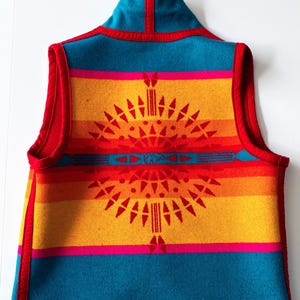 May include: A sleeveless vest featuring a vibrant gradient of yellow, orange, and red horizontal stripes. The back displays a large, intricate geometric sunburst pattern in red, accented by a central horizontal teal band with a circular motif.