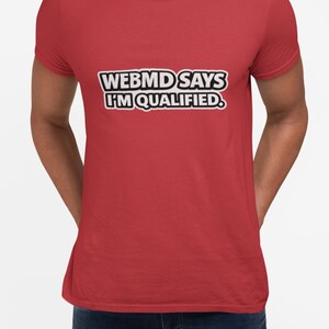 May include: A red t-shirt with the text "WEB MD SAYS I'M QUALIFIED" in a white and black font. The shirt is short-sleeved and appears to be made of a soft material.