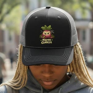 Puede incluir: Gorra de camionero negra con parte trasera de malla y visera curva. La parte delantera presenta un personaje de rábano de dibujos animados y el texto "Farm Goblin" en amarillo. La gorra la lleva una persona.