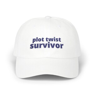 May include: A white baseball cap featuring the text "plot twist survivor" embroidered in dark blue thread across the front panel. The cap has a structured crown, a curved brim, and a button at the top centre, providing a clean and simple design.