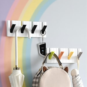 May include: White wall-mounted coat rack with four black hooks. An umbrella, keys, a purse, and other items hang from the hooks. The background features a rainbow gradient.