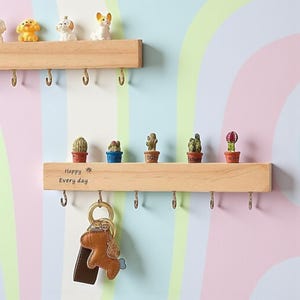 May include: Wooden wall-mounted key holder with small hooks. The shelf displays miniature dog figurines and potted cacti. A leather dog keychain hangs from one hook. The text "Happy Every day" is printed on the shelf.