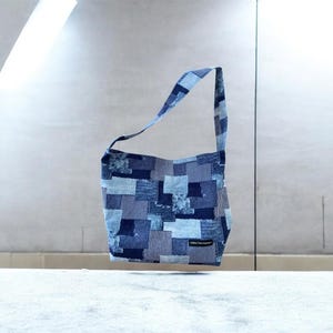 May include: A patchwork denim shoulder bag in various shades of blue. The bag has a rectangular body and a long strap. The denim is pieced together in a random pattern. A small label is sewn on the front.