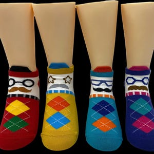 May include: Four pairs of novelty socks on display. Each pair features a different design: eyeglasses and a mustache, stars and a mustache, eyeglasses and a mustache, and eyeglasses and a mustache. The socks have argyle patterns in various colors, including red, yellow, teal, and blue.