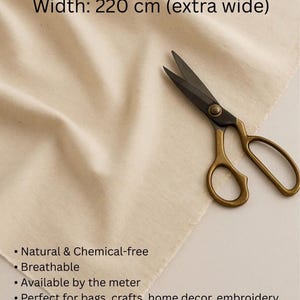 May include: Cream-coloured cotton fabric with text: "%100 Cotton, Width: 220 cm (extra wide)". Features include "Natural & Chemical-free" and "Breathable". A pair of scissors with gold handles and black blades rests on the fabric.