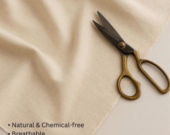 May include: Cream-colored cotton fabric with text: "%100 Cotton, Width: 220 cm (extra wide)". Features include "Natural & Chemical-free" and "Breathable". A pair of scissors with gold handles and black blades rests on the fabric.