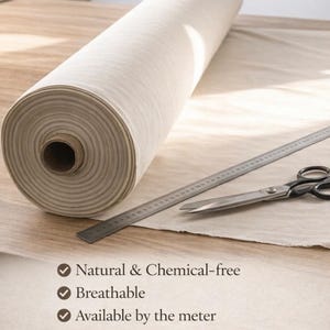 May include: A roll of natural-colored fabric sits on a wooden surface, accompanied by a metal ruler and scissors. The fabric is labeled as natural, chemical-free, and breathable, available by the meter. It is suitable for bags, crafts, home decor, embroidery, curtains, and DIY projects.