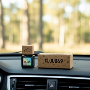 以下が含まれることがあります： 雲のデザインが施された木製のトップが付いた車の芳香剤と、「CLOUD69」の文字が入った箱。芳香剤には「$2 TREE UPGRADE」と書かれたホログラフィックラベルが付いています。商品は車のダッシュボードにあります。