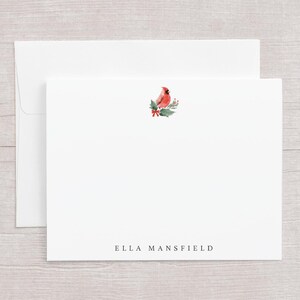 May include: White stationery set featuring a watercolor cardinal bird design with holly and a red bow. The set includes a folded card and an envelope. The name "ELLA MANSFIELD" is printed in a simple font at the bottom of the card.