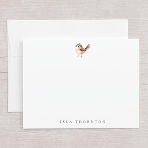 May include: White stationery set featuring a watercolor illustration of a small bird. The set includes a folded card and an envelope. The name "ISLA THORNTON" is printed in a simple font at the bottom of the card.