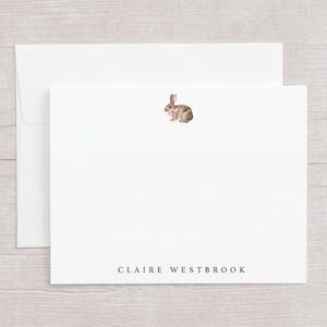 May include: White stationery set featuring a watercolor illustration of a bunny with a pink bow. The set includes a folded card and an envelope. The name "CLAIRE WESTBROOK" is printed in a simple font at the bottom of the card.