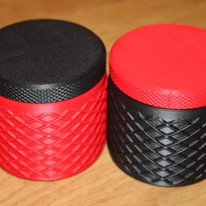 Peut inclure: Deux récipients cylindriques avec des motifs en losanges texturés. L'un est rouge avec un dessus noir, l'autre est noir avec un dessus rouge. Les dessus sont plats et les côtés ont un motif de losange répétitif.