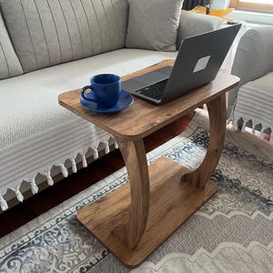 Puede incluir: Una mesa auxiliar de madera con un port&aacute;til y una taza y un platillo azules. La mesa tiene un acabado de veta de madera marr&oacute;n claro y un dise&ntilde;o de patas curvas. La mesa mide 61 cm de largo, 30 cm de ancho y 61 cm de alto.