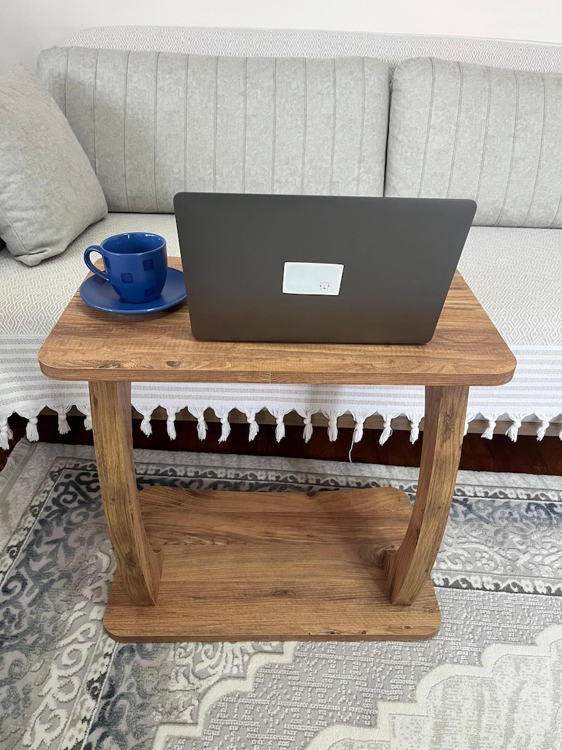 Puede incluir: Una peque&ntilde;a mesa auxiliar de madera con un port&aacute;til y una taza y un platillo azules. La mesa tiene un acabado marr&oacute;n c&aacute;lido y un estante inferior. El port&aacute;til es negro y est&aacute; abierto, y la taza y el platillo son de un azul vibrante.
