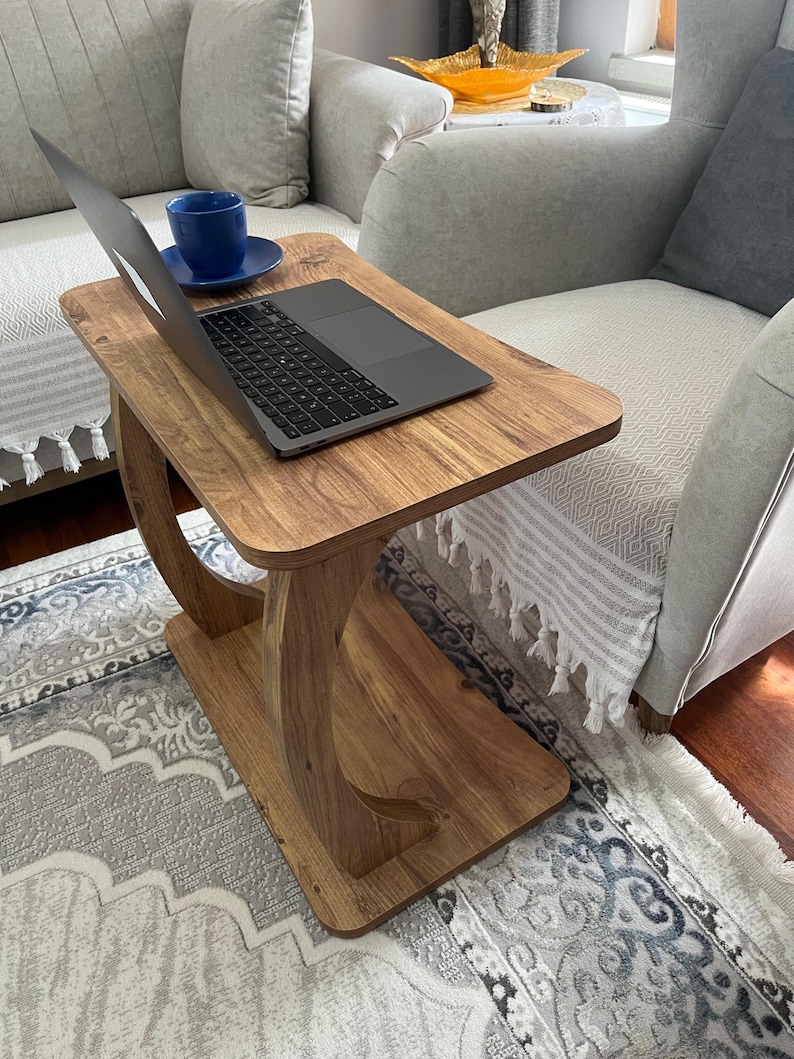 Puede incluir: Una mesa auxiliar de madera con un port&aacute;til y una taza de t&eacute; azul y un platillo. La mesa tiene un acabado marr&oacute;n claro y un dise&ntilde;o de pata curvada &uacute;nico. El port&aacute;til est&aacute; abierto, mostrando una pantalla oscura.