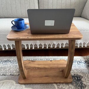 Puede incluir: Una peque&ntilde;a mesa auxiliar de madera con un port&aacute;til y una taza y un platillo azules. La mesa tiene un estante inferior y patas curvas. El port&aacute;til est&aacute; cerrado y tiene una pegatina blanca en la parte trasera.