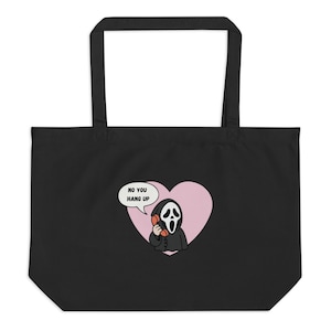 May include: A black tote bag featuring a graphic of a masked figure in a black robe holding an orange telephone receiver. Behind the figure is a light pink heart shape and a speech bubble containing the black text, NO YOU HANG UP.
