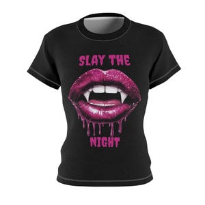 Könnte beinhalten: Schwarzes T-Shirt mit einer Grafik von rosa Lippen mit Fangzähnen und den Worten "SLAY THE NIGHT" in Pink. Die Lippen haben einen tropfenden Effekt. Das T-Shirt hat kurze Ärmel und einen Rundhalsausschnitt. Ein auffälliges Design.