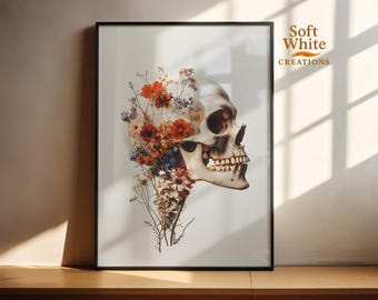 May include: Framed art print featuring a detailed illustration of a human skull intertwined with colorful flowers. The artwork includes orange, red, and blue floral elements. The print is set against a neutral background and framed in a black frame. The text "Soft White Creations" is visible.