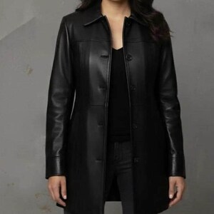 May include: A black leather coat with a collared neckline and button-down closure. The coat has long sleeves and a tailored fit, reaching to mid-thigh. The coat is a solid black color and appears to be made of genuine leather.