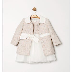 May include: A light-colored tweed coat with a white collar and trim, paired with a white dress featuring a tulle skirt and a bow at the waist. The coat has two buttons and is hanging on a wooden hanger.