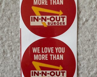 May include: Two red, circular stickers with the text "WE LOVE YOU MORE THAN" above the "IN-N-OUT BURGER" logo. The logo features a yellow arrow. The text "1 sheet/2 stickers" is at the bottom.
