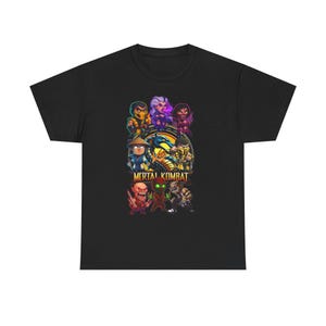 Könnte beinhalten: Ein schwarzes Kurzarm-T-Shirt mit einem farbenfrohen Grafikdruck verschiedener Mortal Kombat-Charaktere im Chibi-Stil. Das Design enthält den Mortal Kombat-Logo-Schriftzug am unteren Rand und ein zentrales Drachenemblem mit den Buchstaben VS.