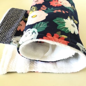May include: A set of handmade oven mitts and a towel. The oven mitts feature a navy blue floral pattern with pink and white flowers and green leaves. The interior is white. The towel is white with a textured pattern and a black and white patterned border.