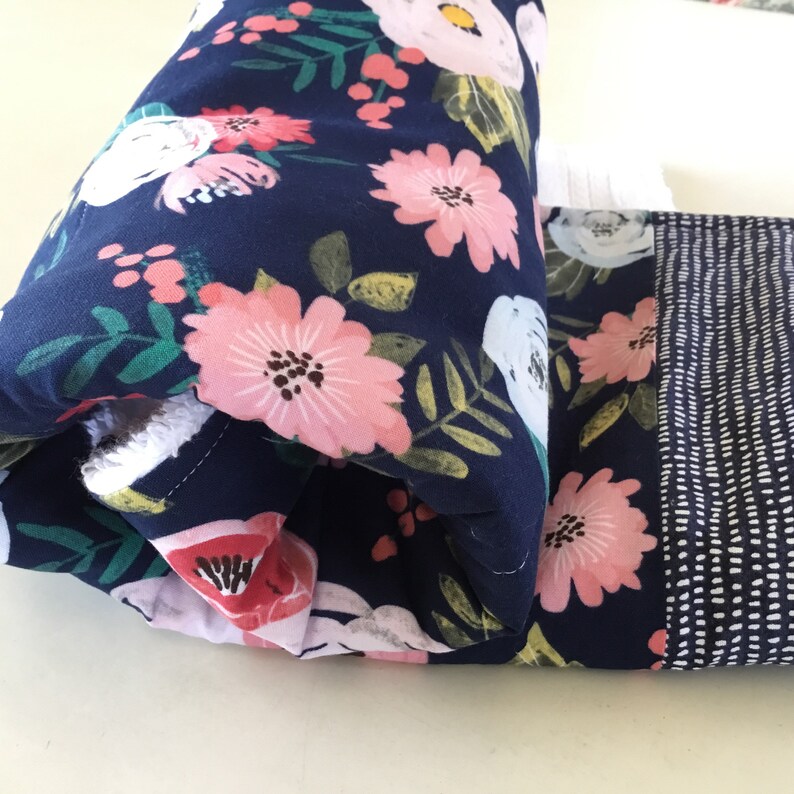 May include: Close-up of a folded fabric item featuring a navy blue floral pattern with pink and white flowers and green leaves. The item also has a section with a white dotted pattern on a navy blue background.