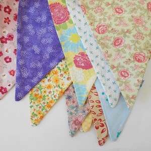 May include: A bunting banner with eight triangular flags in various floral patterns. The flags are made of fabric and feature different colors, including pink, purple, yellow, and blue.