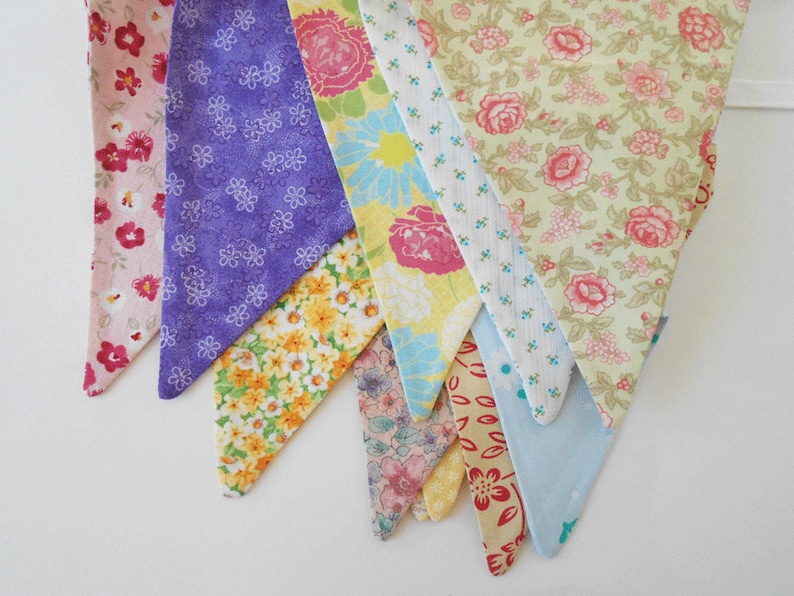 May include: A bunting banner with eight triangular flags in various floral patterns. The flags are made of fabric and feature different colors, including pink, purple, yellow, and blue.