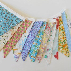 May include: A bunting banner with 10 triangular flags. The flags are made of different fabrics with floral patterns in shades of blue, yellow, pink, and green.