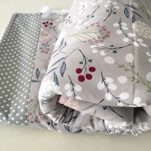 May include: A gray and white floral print baby blanket with a gray polka dot border. The blanket is folded in half and has a soft, fluffy texture.