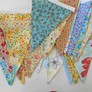 May include: A collection of colorful fabric bunting flags with floral patterns. The flags are sewn together with white ribbon and have a white lace trim.