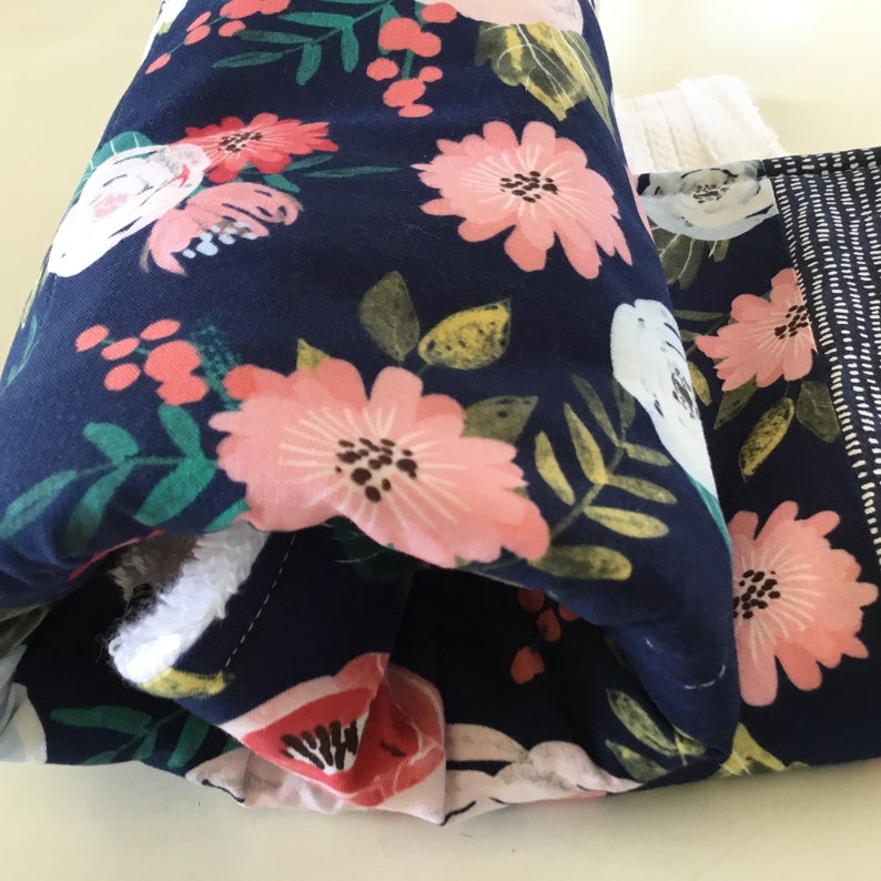 May include: Close-up of two fabric items with a navy blue floral pattern. The pattern features large pink and white flowers with green leaves. One item has a white, textured edge, and the other has a white dotted pattern on the side.