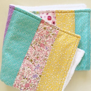 May include: A multi-colored baby burp cloth with a white terry cloth backing. The fabric is a patchwork of turquoise, yellow, and pink floral patterns.