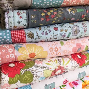 May include: A stack of folded, colorful fabric quilts. Each quilt features a patchwork design with floral and geometric patterns in shades of pink, green, yellow, and blue. The quilts are neatly stacked, showcasing the variety of designs.