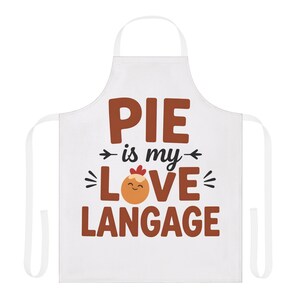 May include: White apron with the text "PIE is my LOVE LANGAGE" in brown letters. The word "LOVE" features a pie graphic with a smiling face. The apron has a neck loop and waist ties.