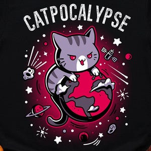 Puede incluir: Una camiseta negra de manga corta con un gráfico de un gato atigrado gris posado sobre un planeta rojo. El texto CATPOCALYPSE está impreso en blanco sobre el gato. El diseño incluye estrellas blancas, un pequeño satélite y un planeta.