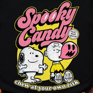Puede incluir: Camiseta negra con un diseño de Halloween. El diseño presenta las palabras "Spooky Candy" en rosa y amarillo, junto con personajes de dibujos animados. También se incluye el texto "chew at your own risk".