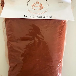 May include: A bag of red iron oxide ceramic supplies. The bag is sealed and has a white label at the top with the text "Kinney Ceramic Supplies" and "Quality Minerals". The label also includes the text "Iron Oxide (Red)".