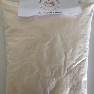 Könnte beinhalten: Ein klarer Plastikbeutel gefüllt mit einem hellbeigen Pulver. Ein weißes Etikett oben zeigt "Kinney Ceramic Supplies Quality Minerals" und "Cornwall Stone". Der Beutel ist versiegelt und voll.