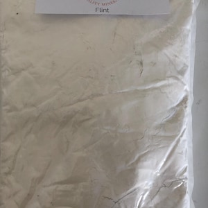 May include: A clear plastic bag filled with a white powder, likely a ceramic material. A white label at the top reads "Kinney Ceramic Supplies, Quality Minerals, Flint" with a small illustration of a ceramic bowl.