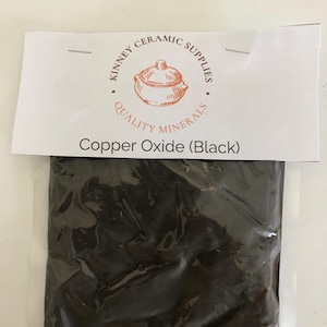 May include: A clear plastic bag containing black copper oxide powder. The bag is sealed at the top with a white label that reads "KINNEY CERAMIC SUPPLIES QUALITY MINERALS" and "Copper Oxide (Black)".