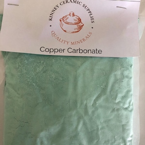 May include: A package of copper carbonate powder, in a light green color. The package has a white label with the text "Kinney Ceramic Supplies" and "Quality Minerals". The product name "Copper Carbonate" is printed on the label.