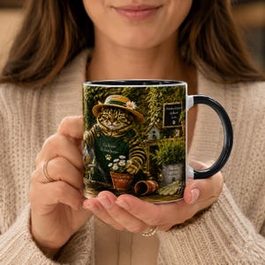 Peut inclure: Un mug en céramique avec une anse et un intérieur noirs, illustré d'un chat tigré portant un chapeau de paille et une salopette verte, arrosant des fleurs. Le texte indique Cultiver le bonheur et Prendre le temps de fleurir avec une patte.