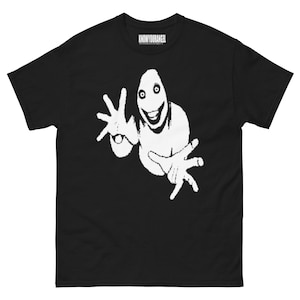 Op de afbeelding: Zwart t-shirt met een witte afbeelding van een lachende, humanoïde figuur met uitgestrekte handen. De tekst "KNOWYOURANGEL" is in het wit op het bovenste deel van het shirt gedrukt.