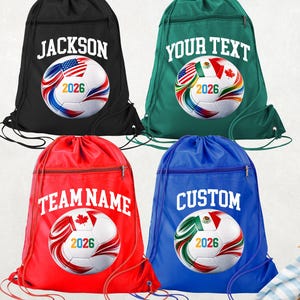 May include: Four drawstring soccer bags in black, green, red, and blue. Each bag features a soccer ball design with a flag and the year 2026. The bags have text that reads "JACKSON", "YOUR TEXT", "TEAM NAME", and "CUSTOM".